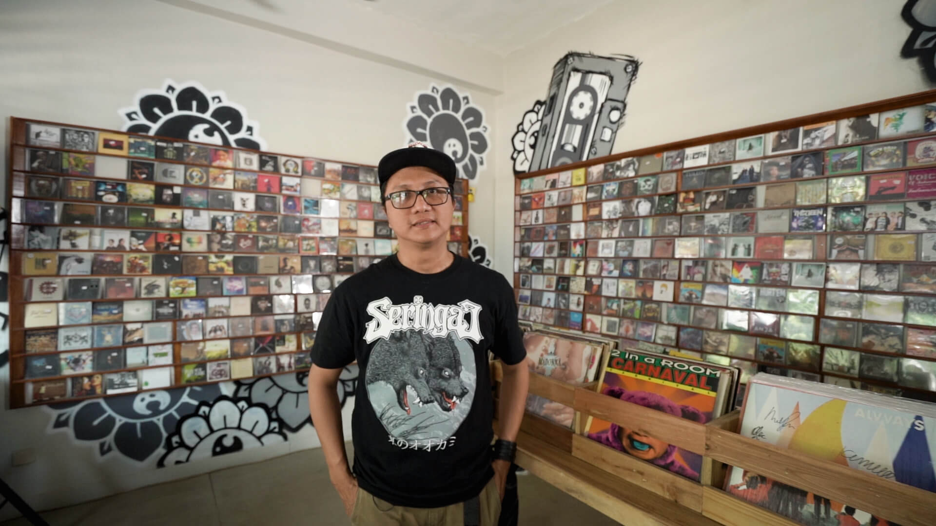 Wendi Putranto menggunakan kaos Seringai berdiri di depan rak cd musik